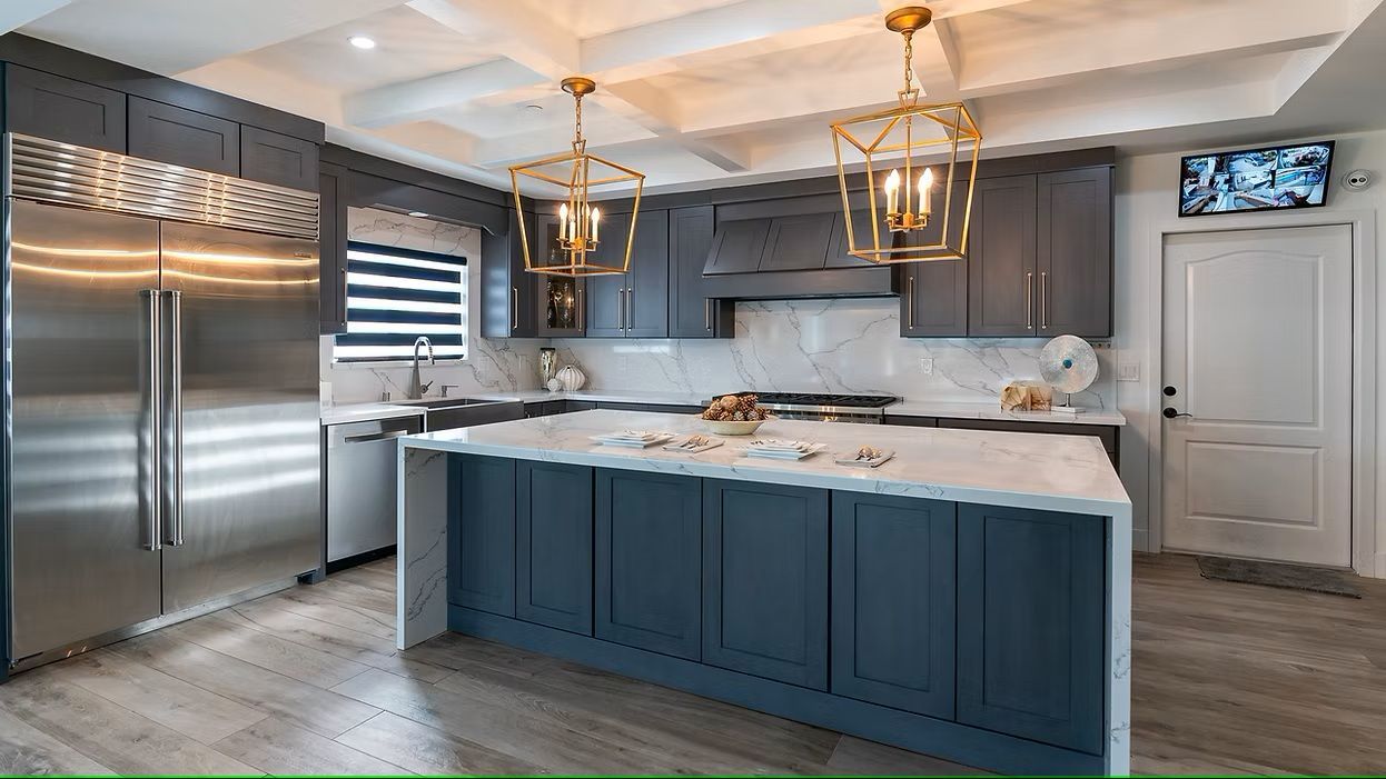 A kitchen with a large island and stools and a stainless steel refrigerator.