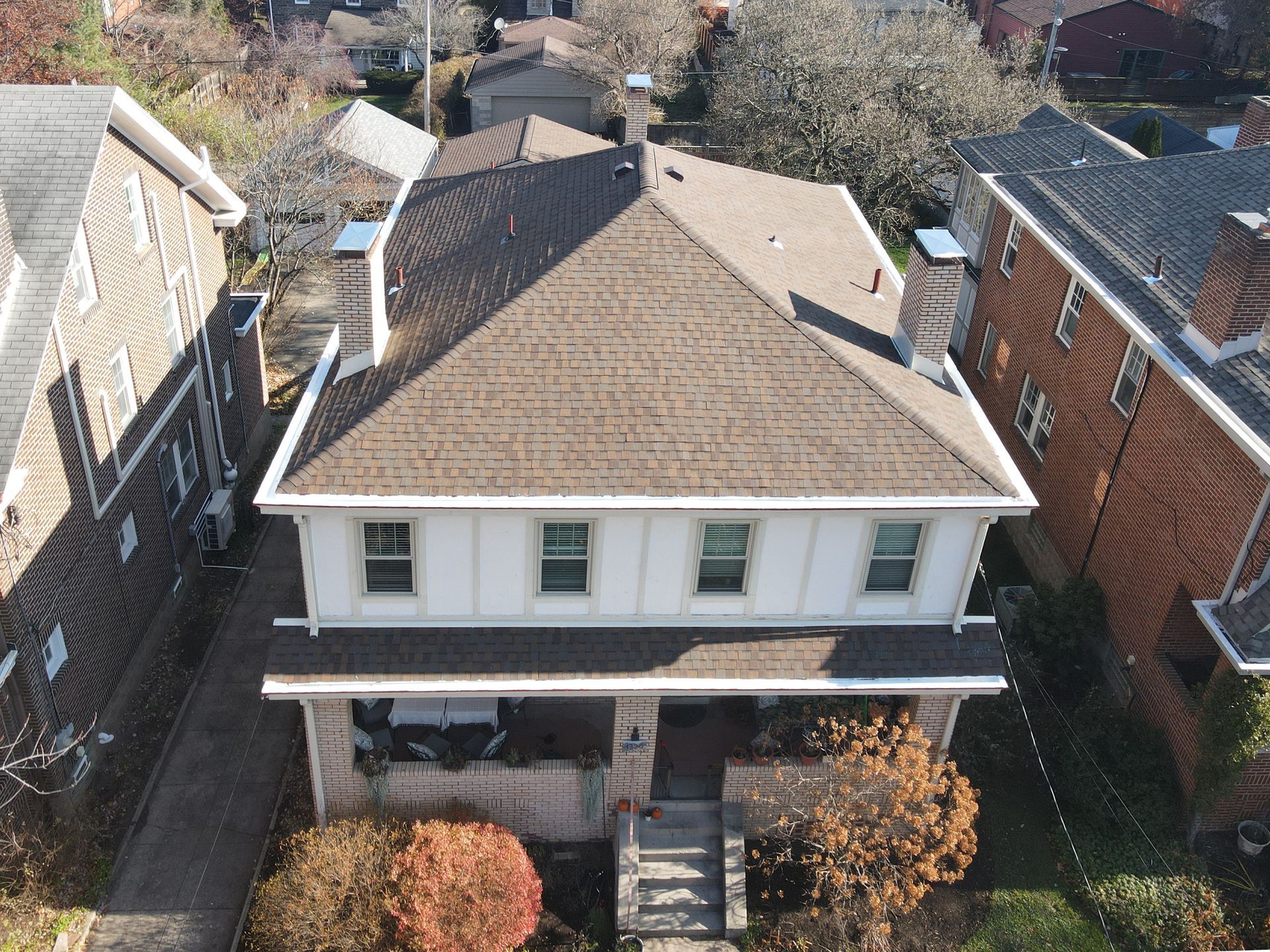 Aerial view of a two-story white house with a brown roof and surrounding homes on a sunny day.