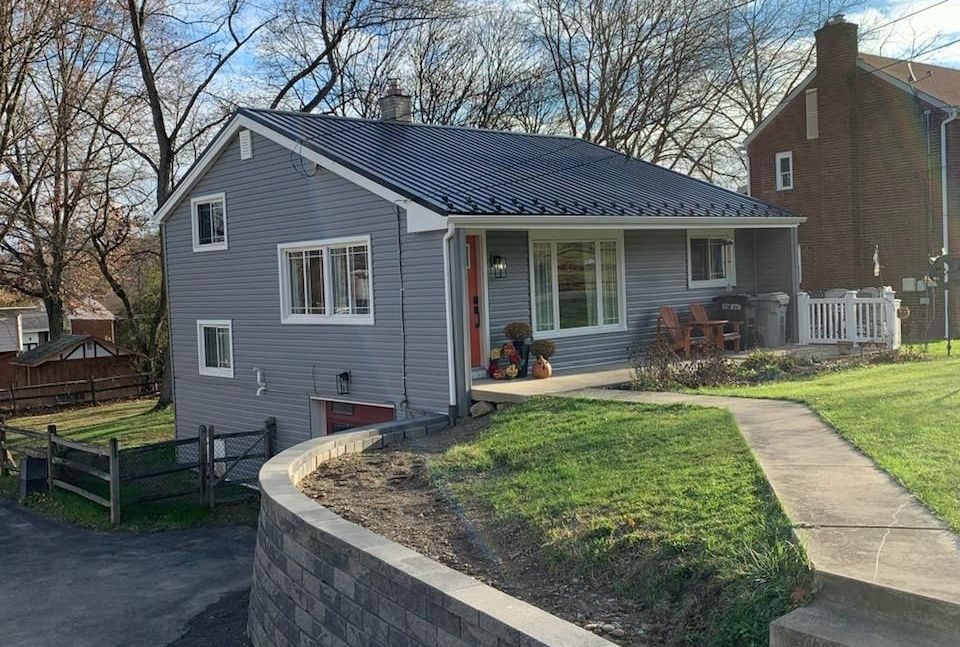 Gray house with a dark blue roof, small front yard, and a stone retaining wall.
