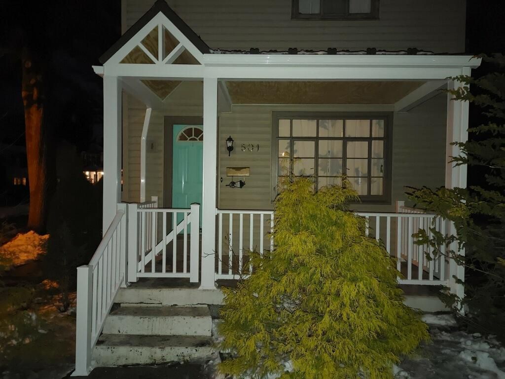 A house front porch at night with a teal door and small evergreen shrub.
