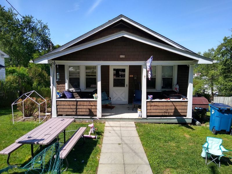 Small brown house with a porch, green yard, and a picnic table. Sunny day.