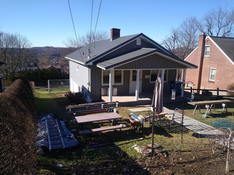 Small gray house with porch, picnic tables in yard, bright sunny day.