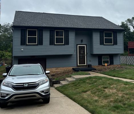 Gray house with black shutters, a dark door, and a silver SUV in the driveway.