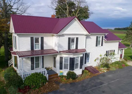 White farmhouse with burgundy metal roof, black shutters, and porch.
