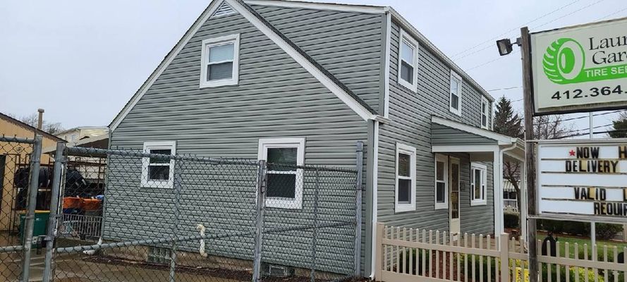 A two-story building with gray siding, chain-link fence, and sign for Laurel Gardens.
