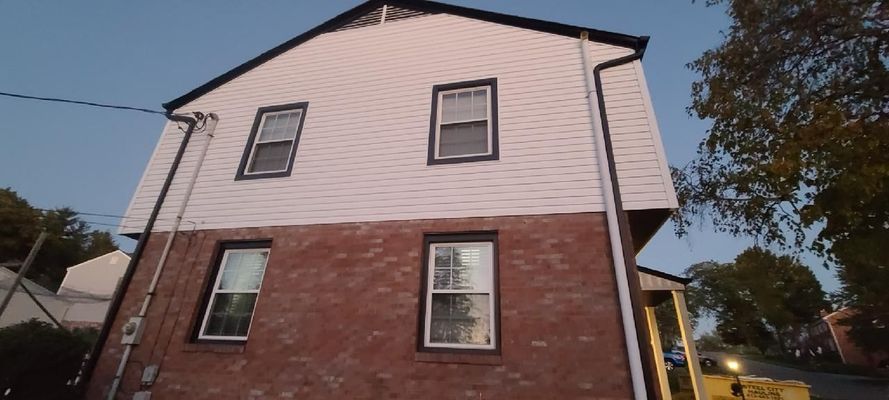 Two-story house with white siding on the upper level and brick on the lower, with dark window frames, set against a blue sky.