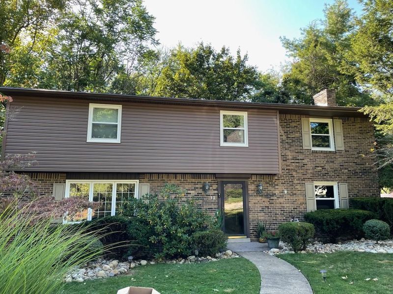 Two-story house with brown siding and brick facade. Windows and a concrete pathway leading to the door.