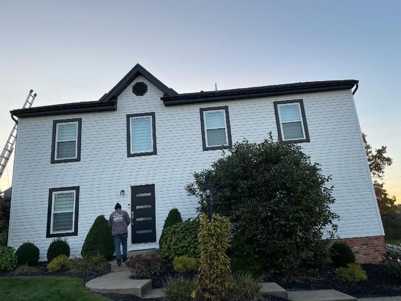 Two-story white house with black trim, a person walking toward the front door, and landscaping.