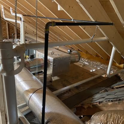 Attic with insulated ductwork, pipes, and wooden rafters under a sloped roof.