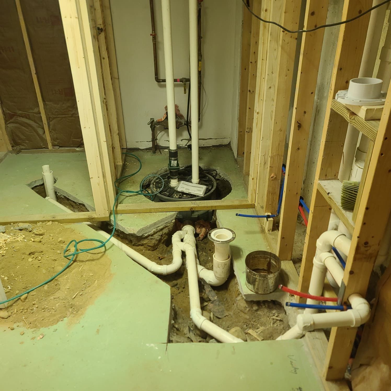 Unfinished bathroom with exposed pipes, open wall studs, and a green subfloor around a shower drain.