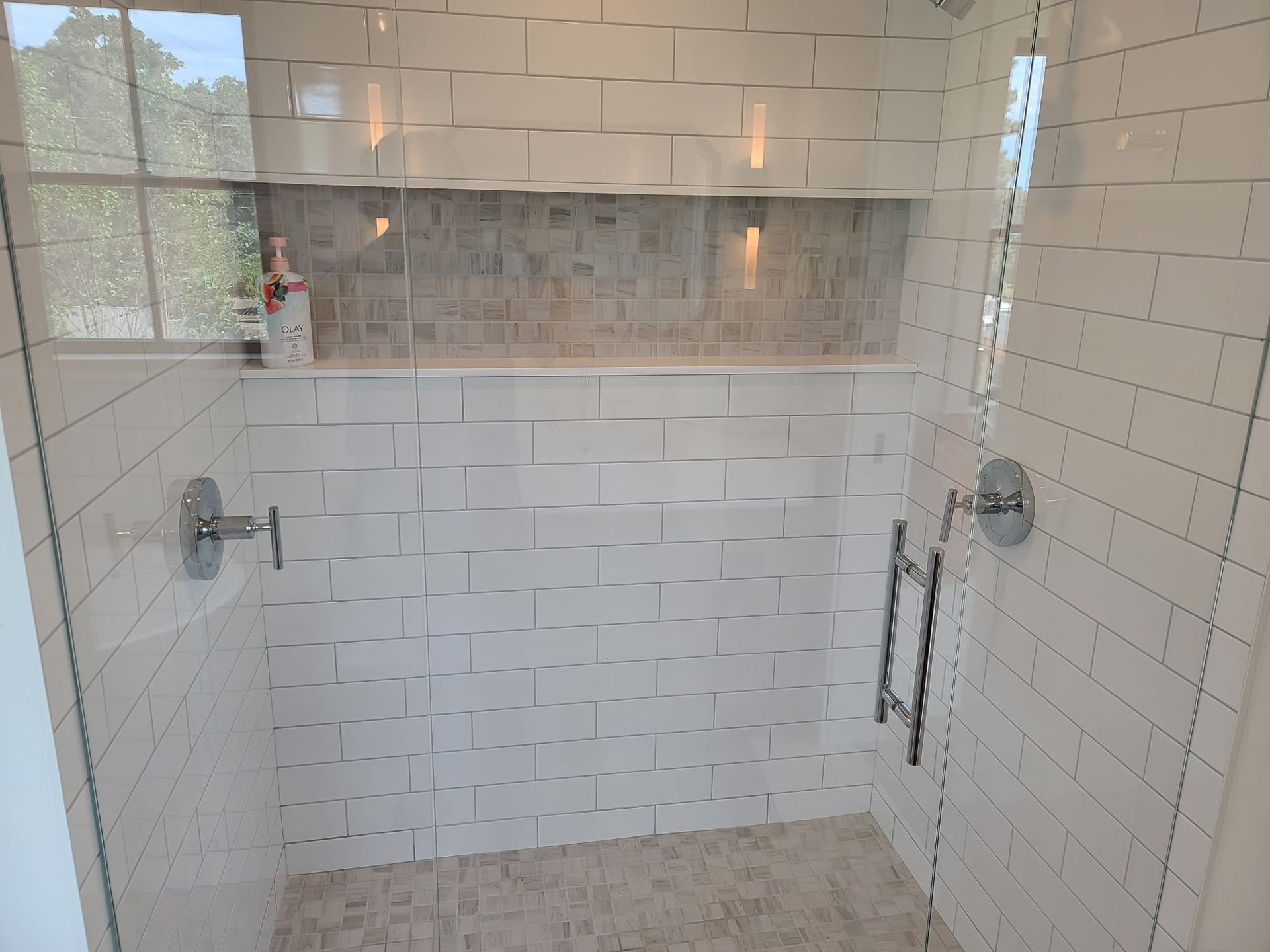 Tiled walk-in shower with glass doors, built-in niche, and beige stone floor