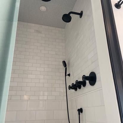 White tiled shower with black fixtures and a handheld showerhead