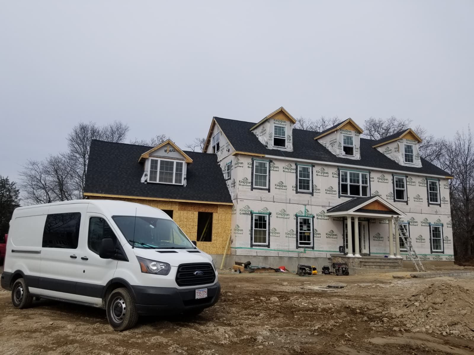 White work van in front of a large house under construction on a muddy lot