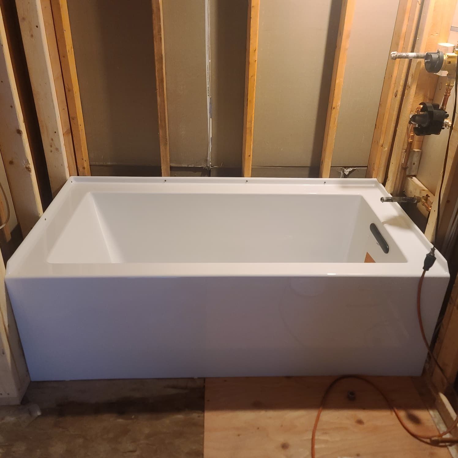 White bathtub installed in an unfinished bathroom with exposed wall studs.