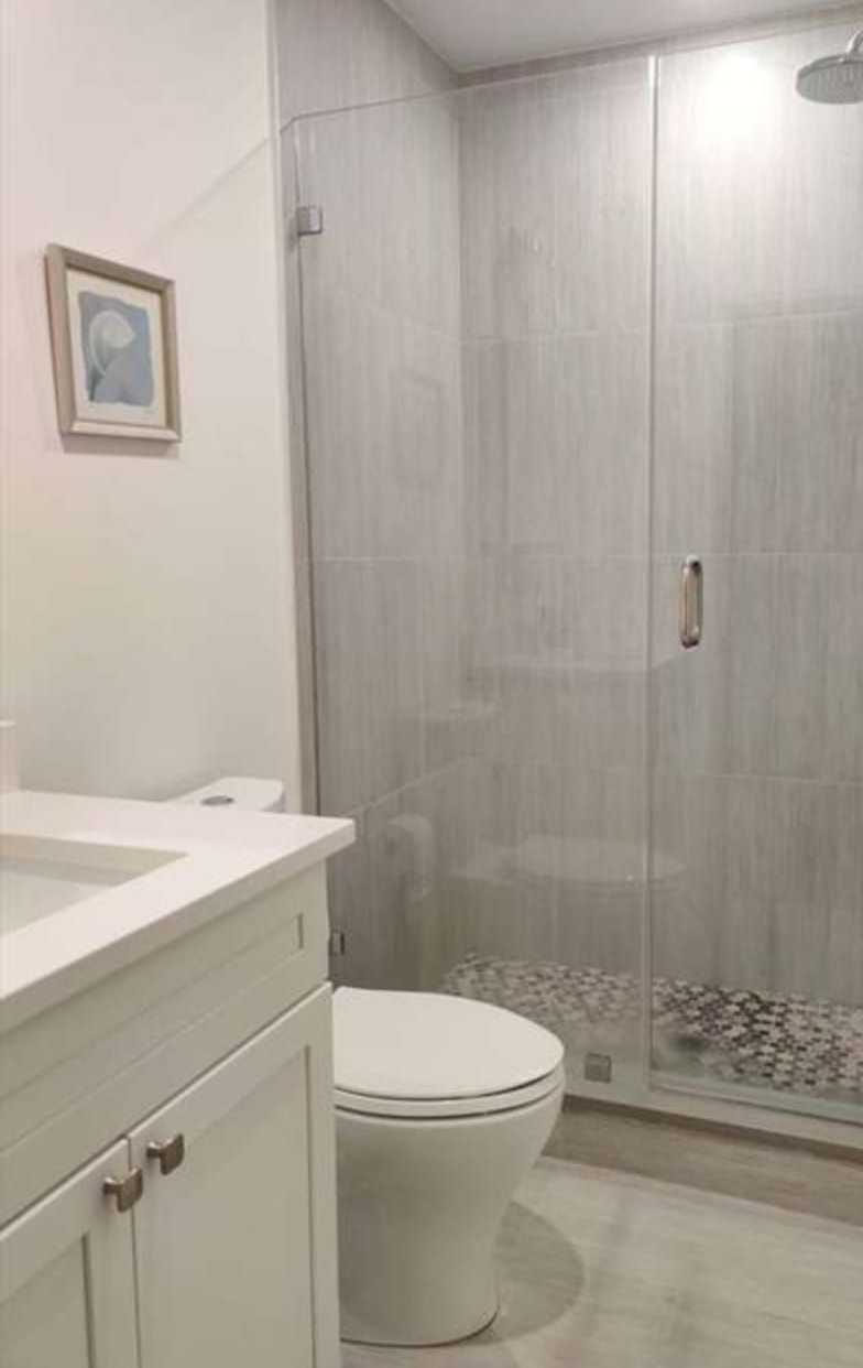 Bathroom with a white toilet, vanity, and glass shower doors with gray tile floor.