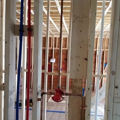 Framed interior wall under construction with exposed studs and plumbing, including a red pipe valve.