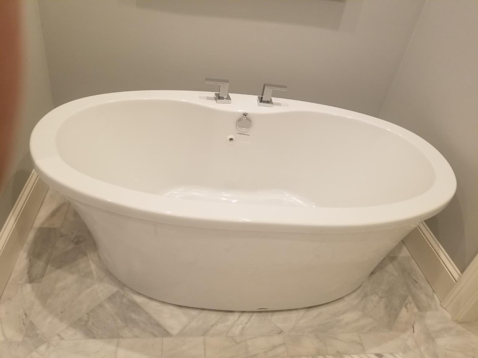 White oval bathtub with chrome fixtures in a tiled bathroom alcove