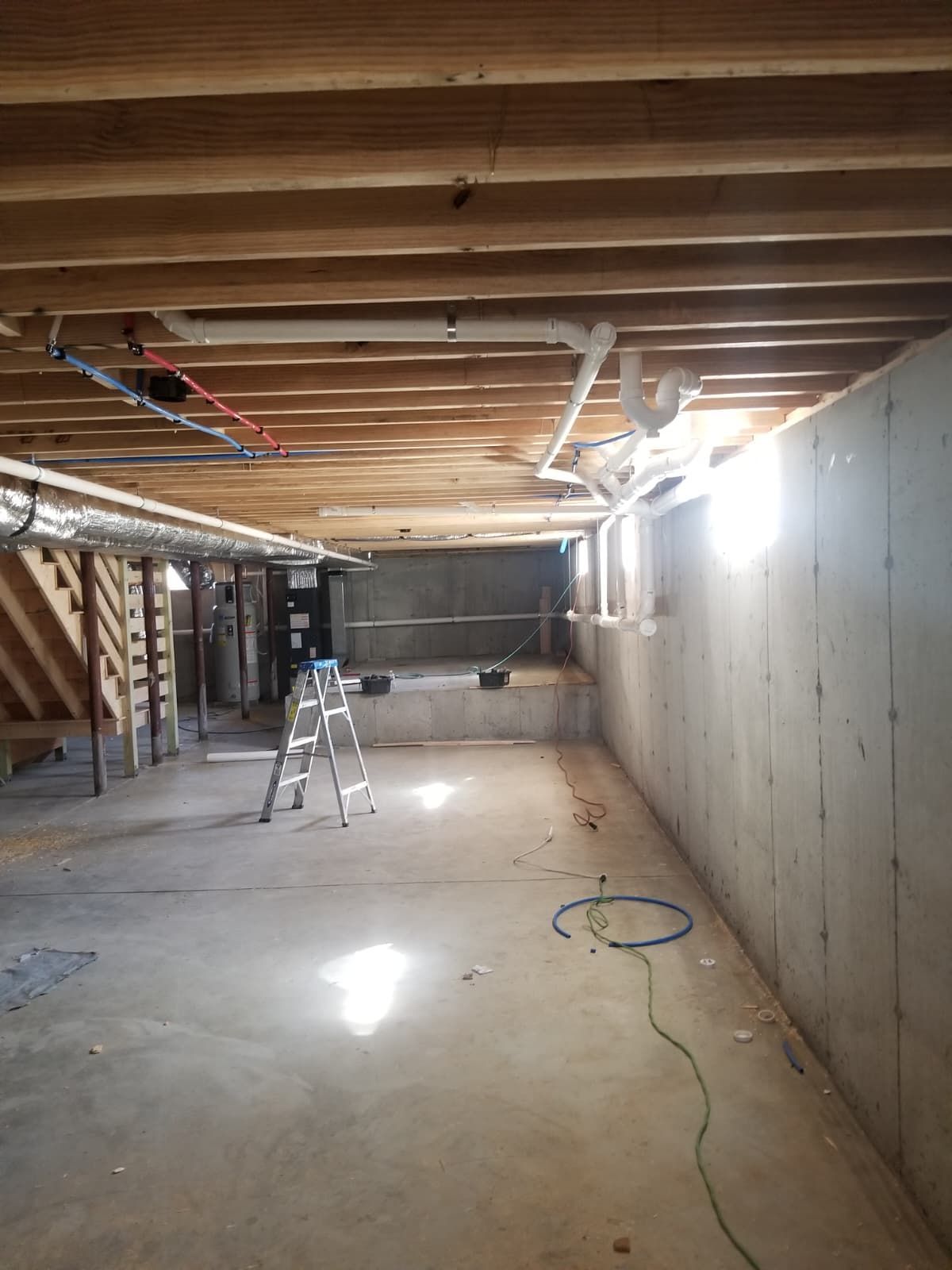 Unfinished basement with exposed ceiling, ladder, tools, and concrete floor under construction.