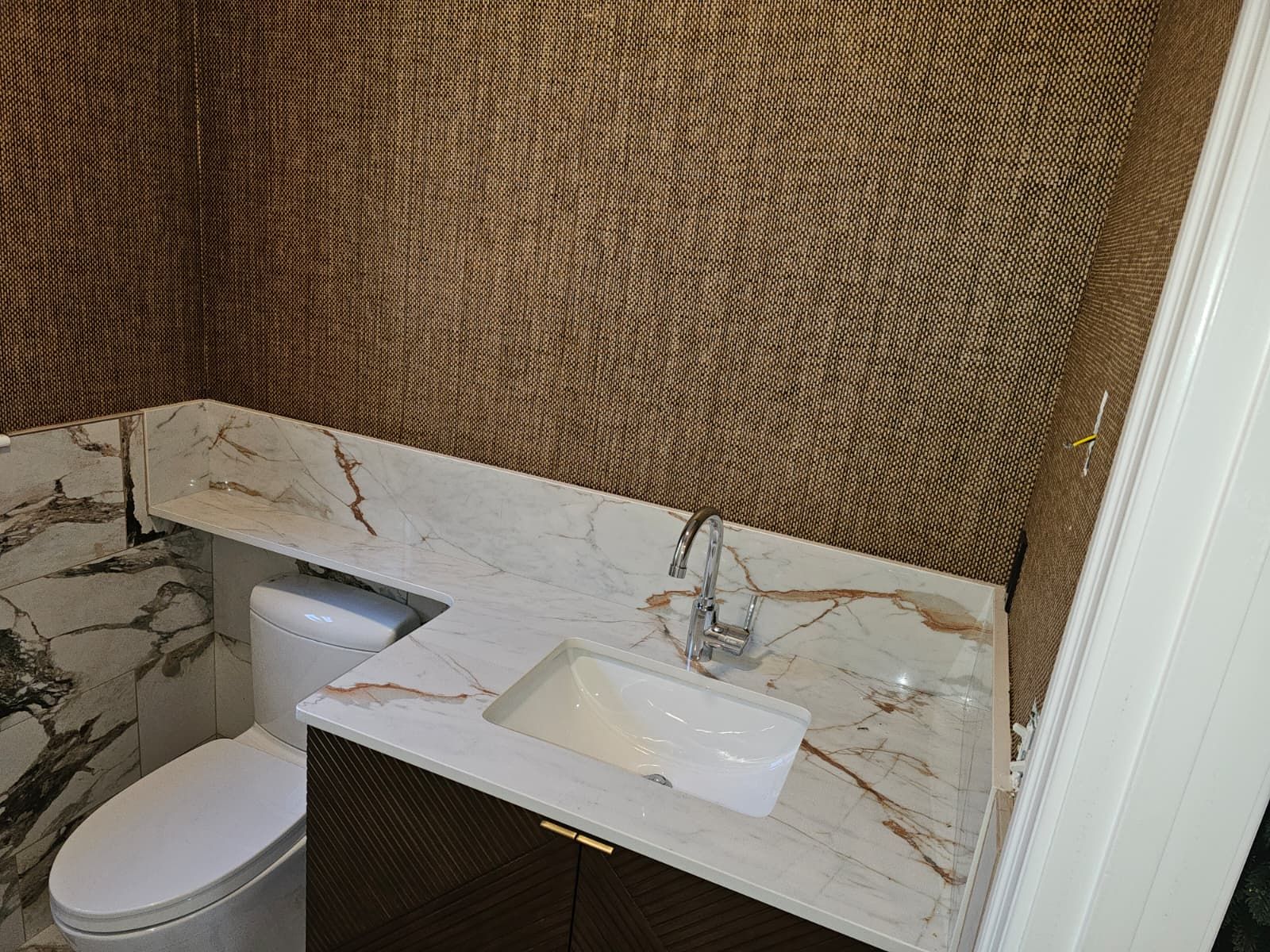 Bathroom vanity with marble countertop, vessel sink, toilet, and woven wall covering