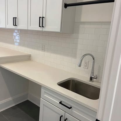 Modern white kitchen with a countertop, subway tile backsplash, and stainless steel sink and faucet