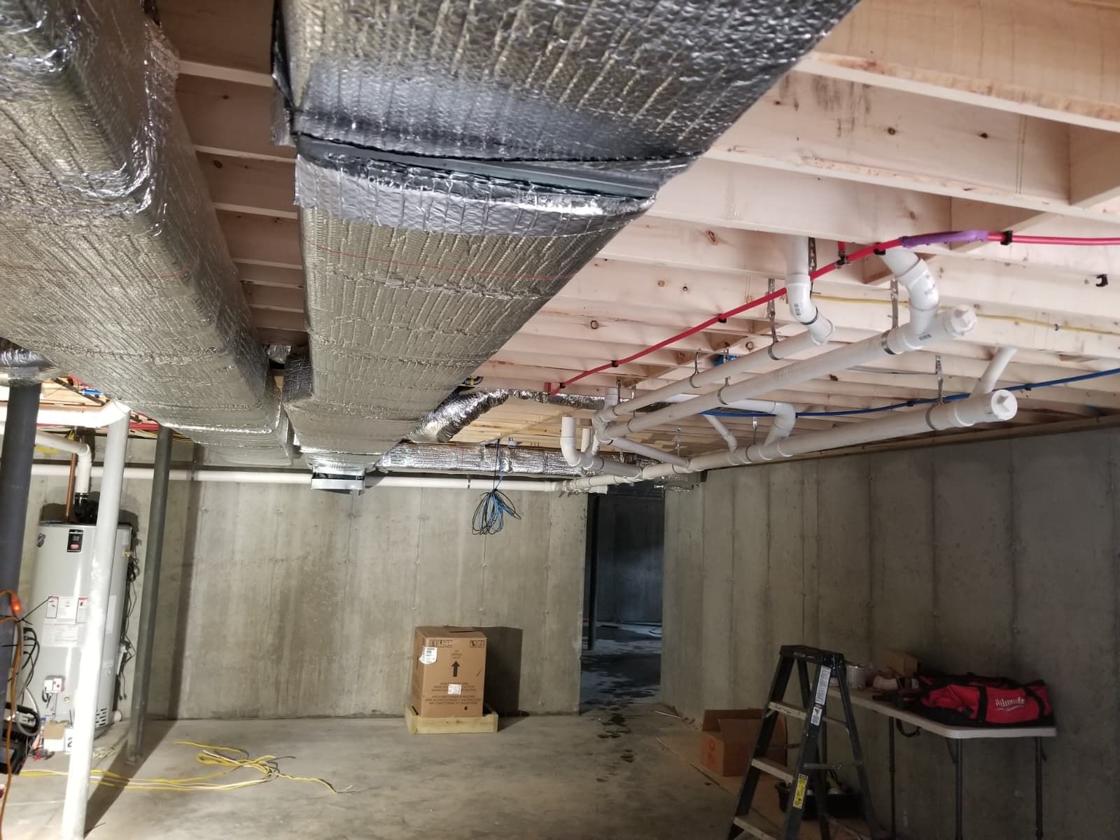 Basement utility room with exposed ducts, pipes, concrete walls, and a small cardboard box on the floor.