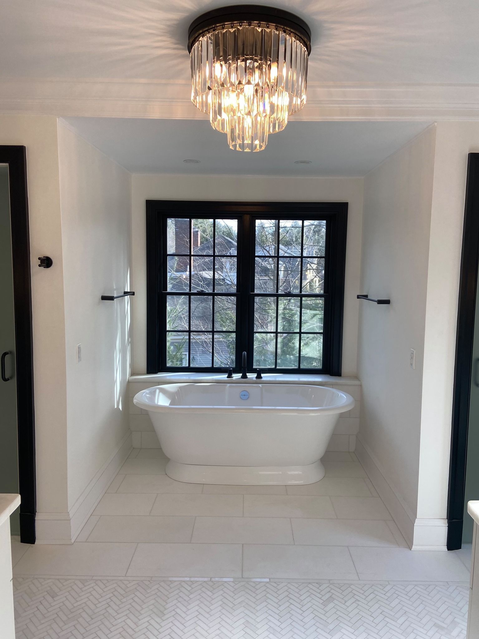 Elegant bathroom with freestanding tub beneath a chandelier and black-framed window