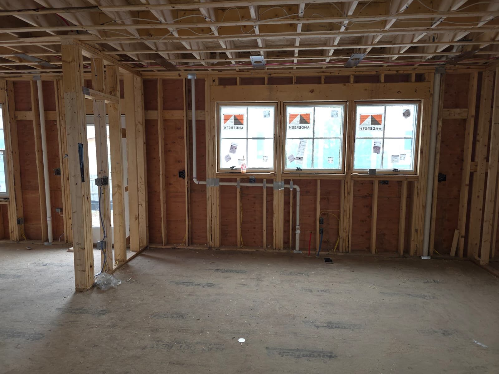 Unfinished interior of a house under construction with exposed wooden framing and windows.