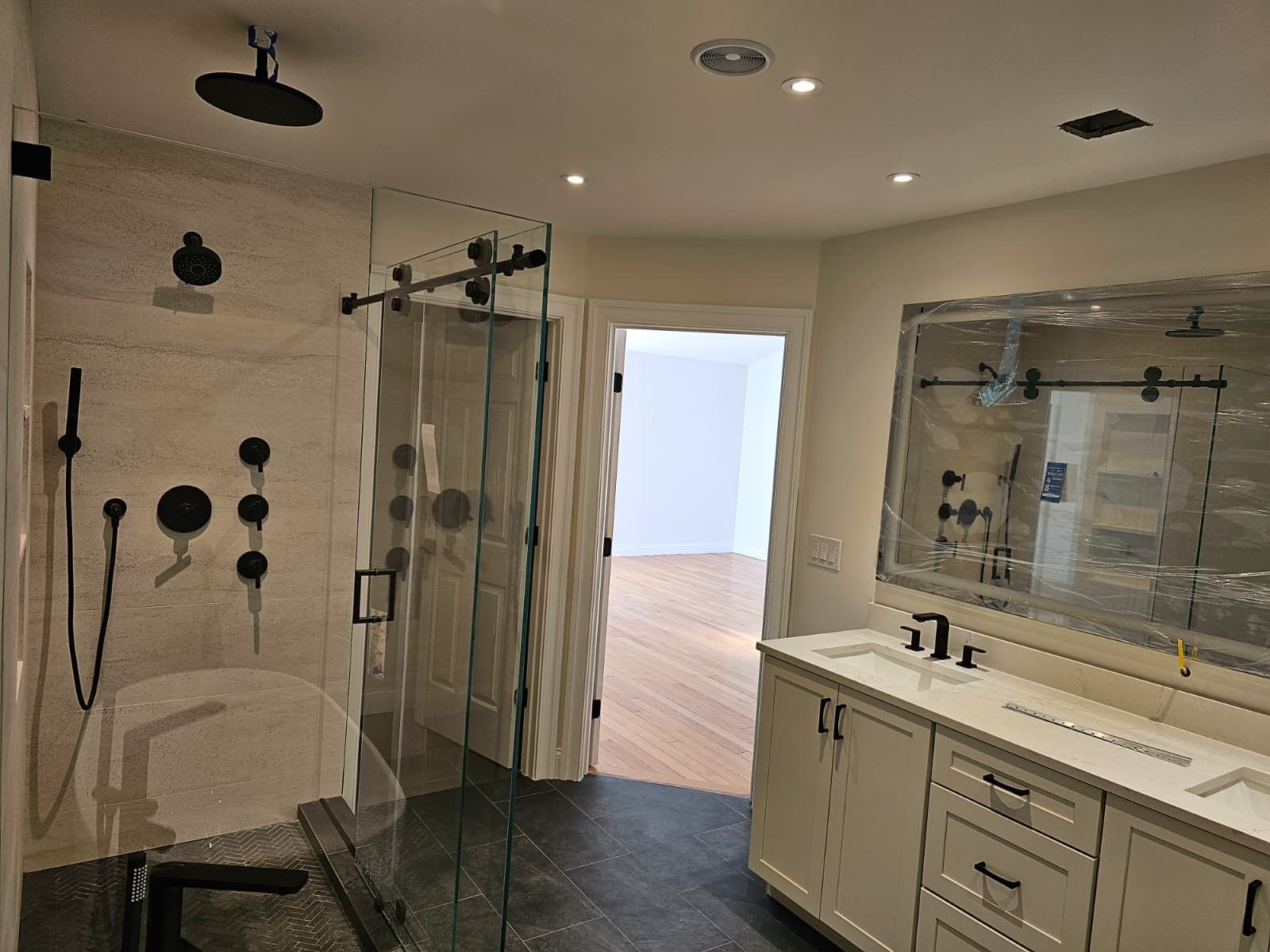 Modern bathroom with glass shower, large mirror, and double vanity in beige tones