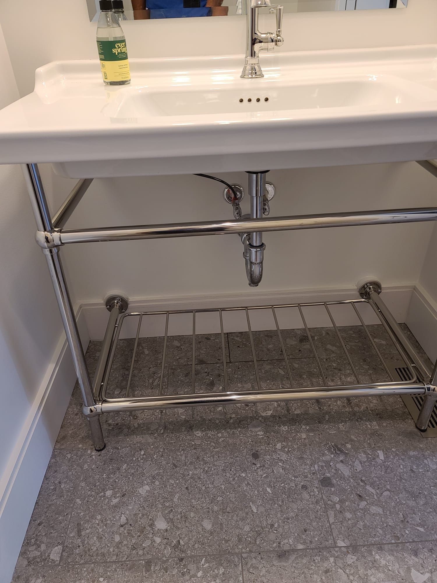 Bathroom sink with chrome metal shelf and towel rack underneath on a tiled floor