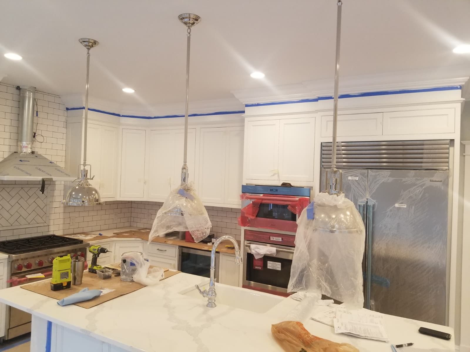 Bright modern kitchen with white cabinets, stainless fridge, island, and hanging pendant lights under renovation