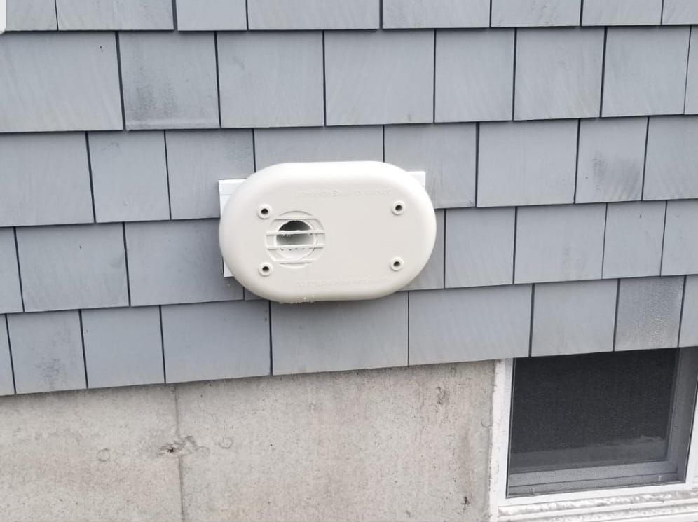 White outdoor utility meter mounted on gray shingle siding above a basement window