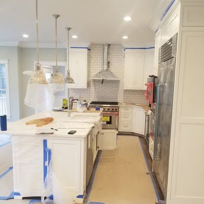 Bright white kitchen with island, pendant lights, stainless fridge, and tiled backsplash