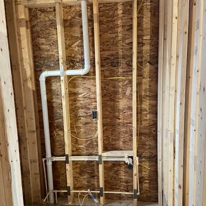 Unfinished wall framing with white PVC pipes and electrical wiring in a construction space