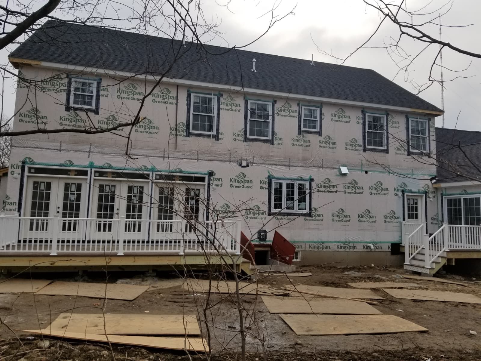 Two-story house under construction with white siding, scaffolding, and a covered porch in front yard