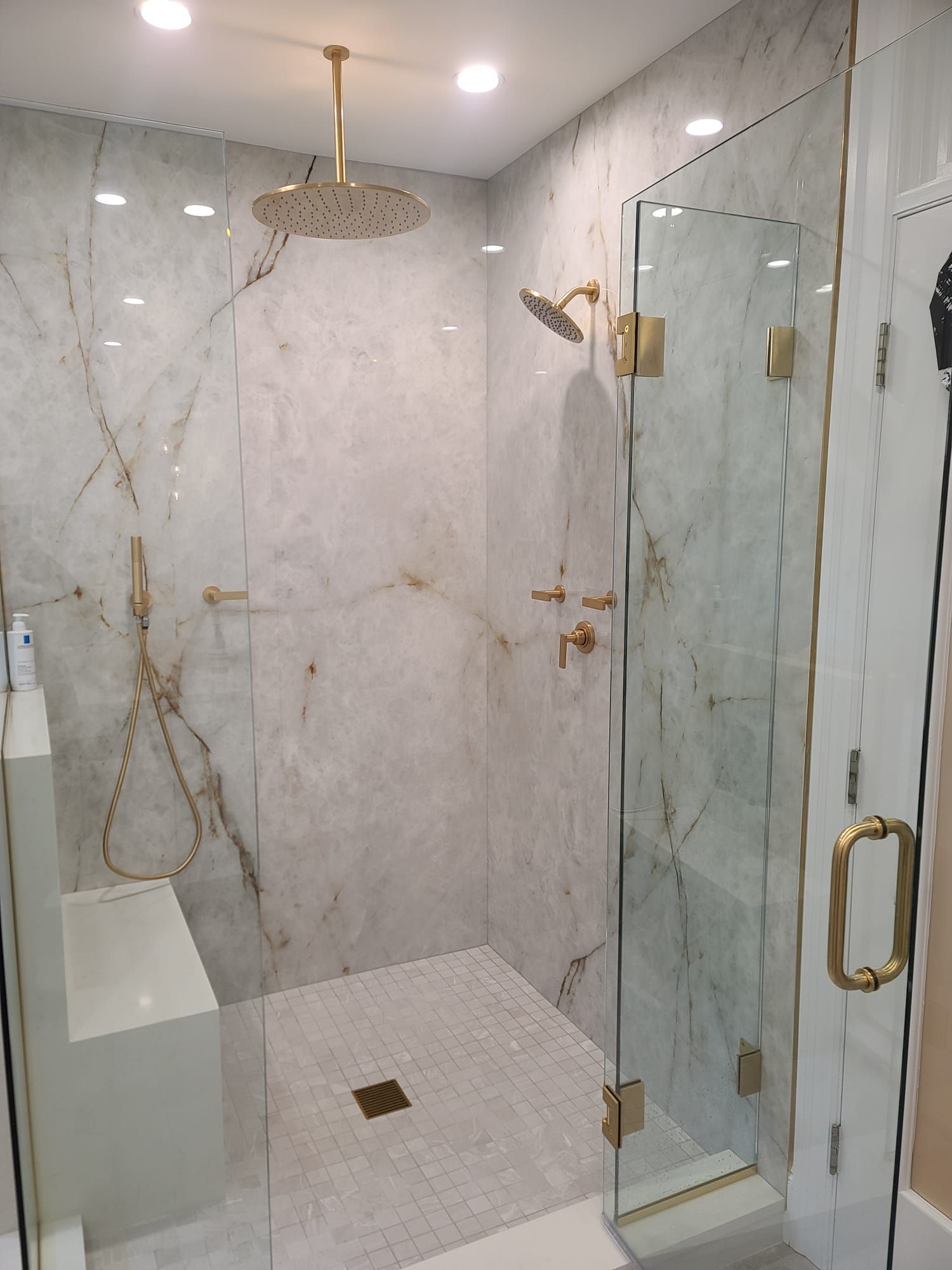 Luxurious marble-tiled shower with glass doors, gold fixtures, and rainfall showerhead