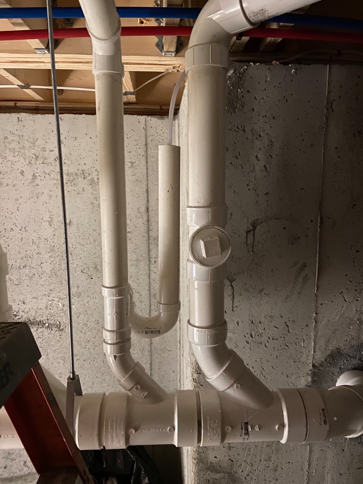 White PVC pipes and elbows on a concrete basement wall with a circular valve handle.