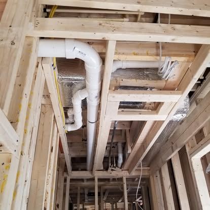 Unfinished house framing with exposed white ductwork and pipes running through the ceiling joists.