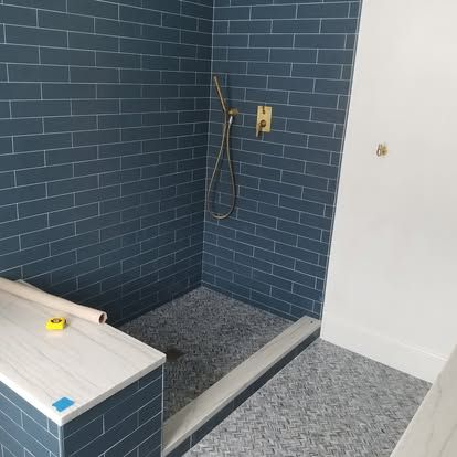 Blue-tiled bathroom corner with a shower curb, exposed plumbing, and a white vanity countertop.