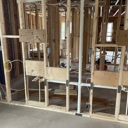 Unfinished interior wall framing in a construction site with exposed studs and plumbing.