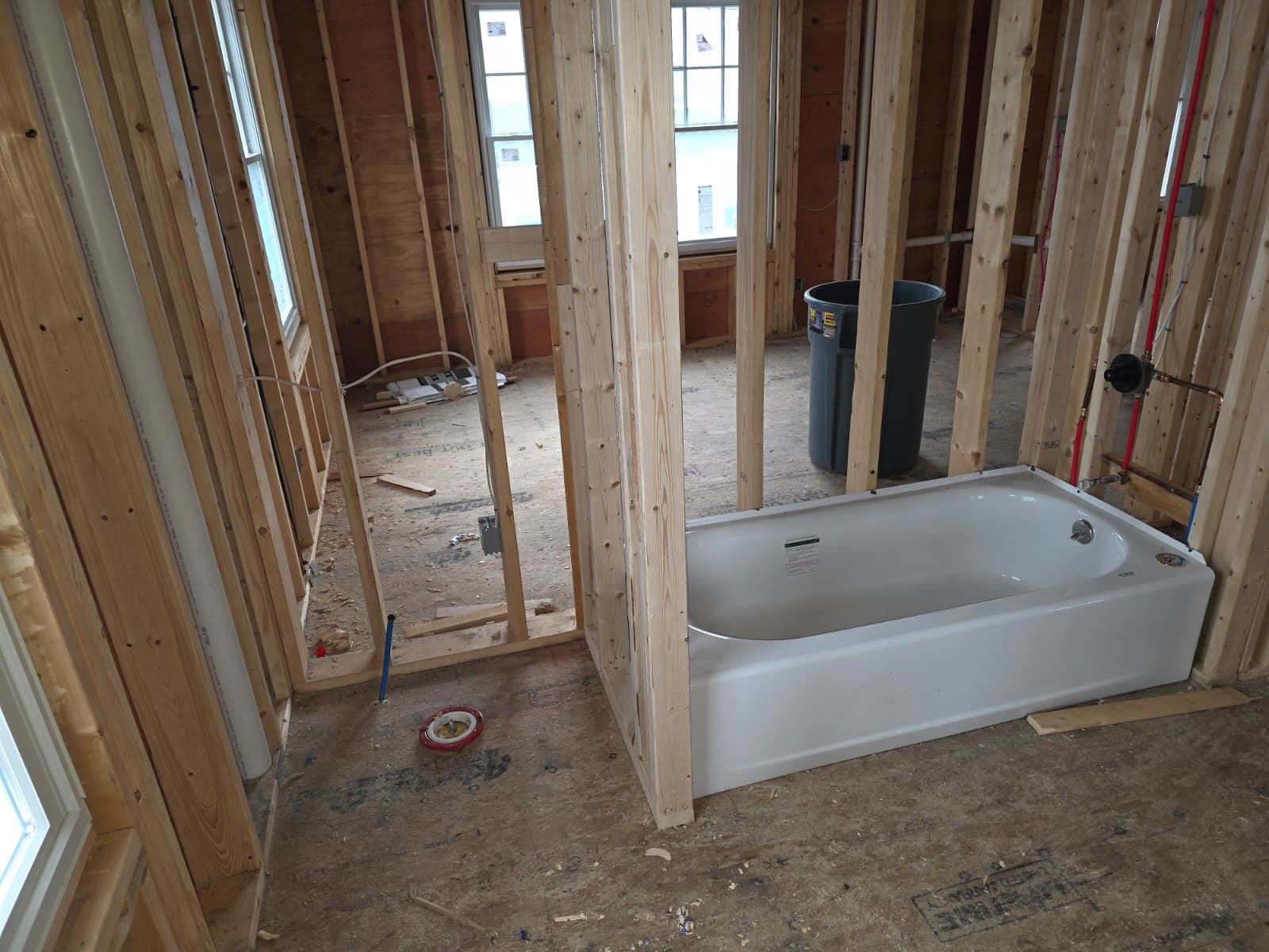 Unfinished bathroom with exposed studs and a white bathtub on the floor.