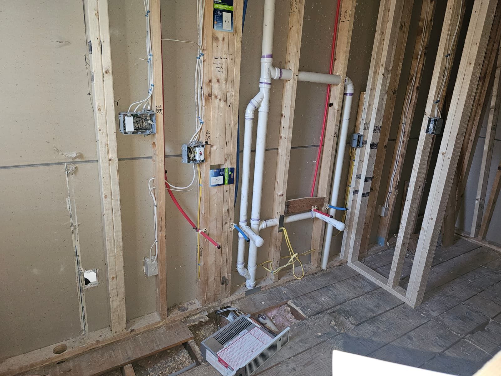 Exposed bathroom wall framing with plumbing pipes, electrical boxes, and a tiled floor during renovation