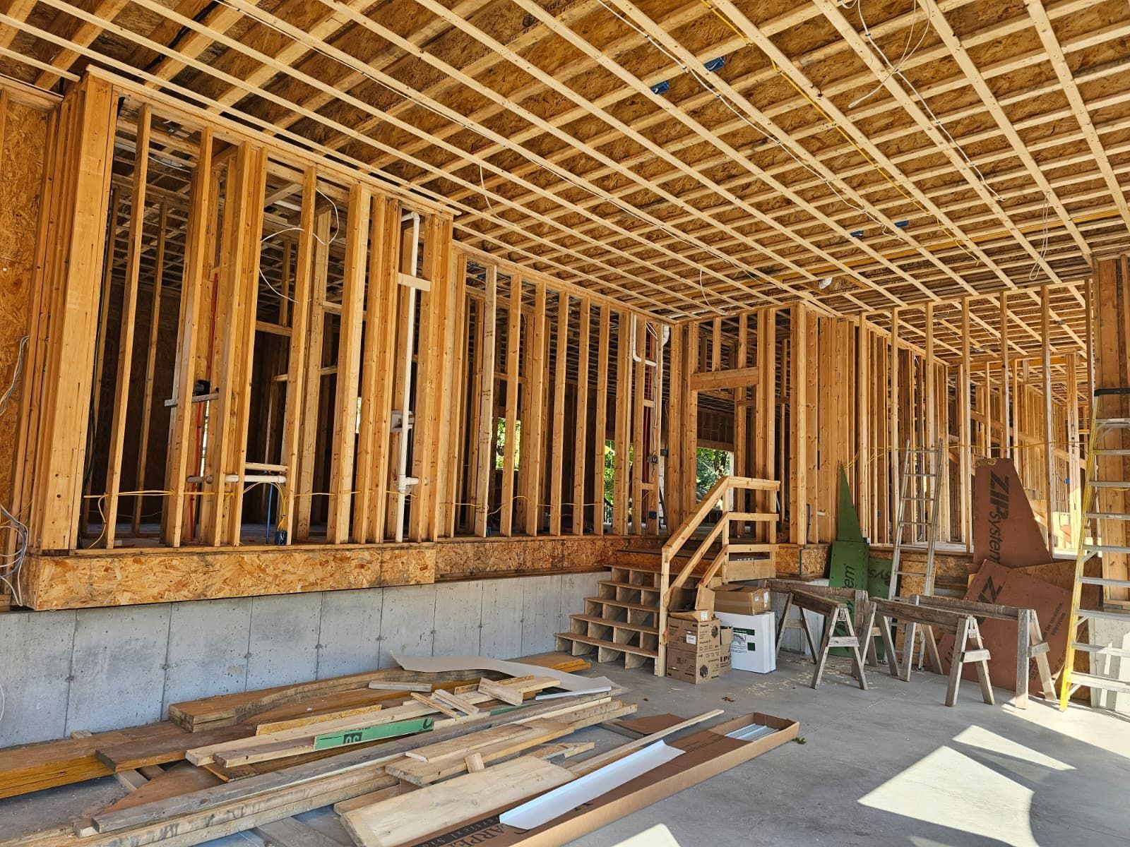 Unfinished house interior with wooden framing, concrete foundation, and construction materials on the floor