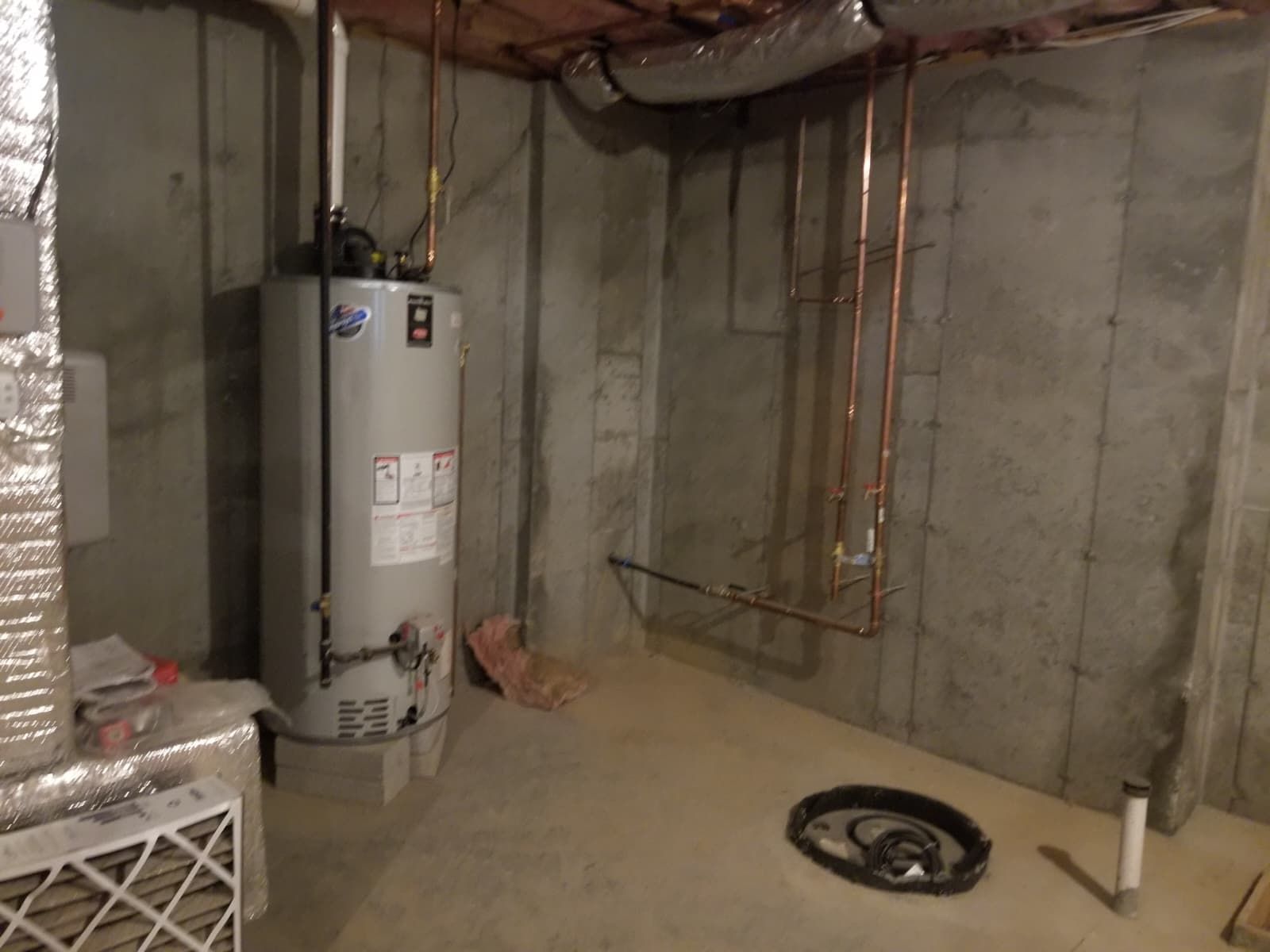 Unfinished basement with water heater, exposed pipes, concrete walls, and a floor drain.