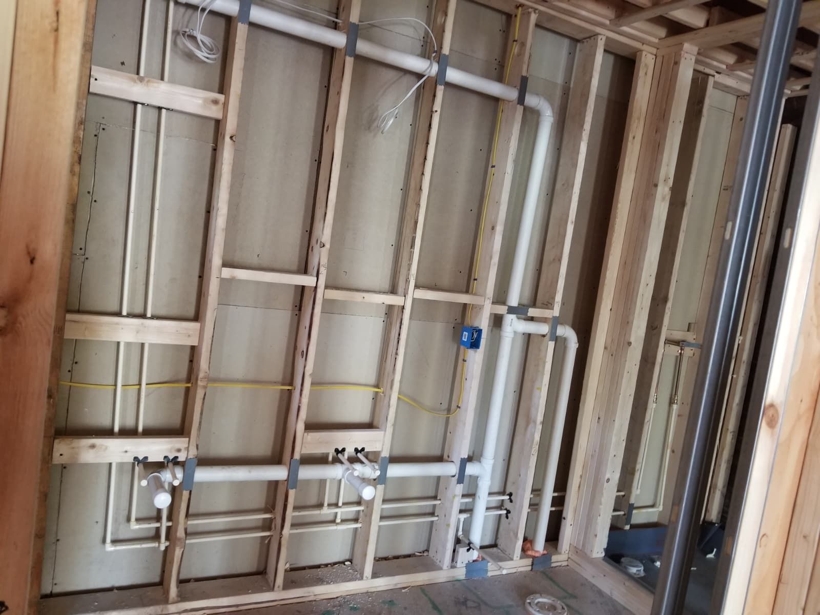 Unfinished bathroom wall with exposed wood framing and plumbing pipes, no drywall installed