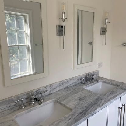 Bathroom vanity with double sinks, gray marble countertop, mirrors, and wall sconces