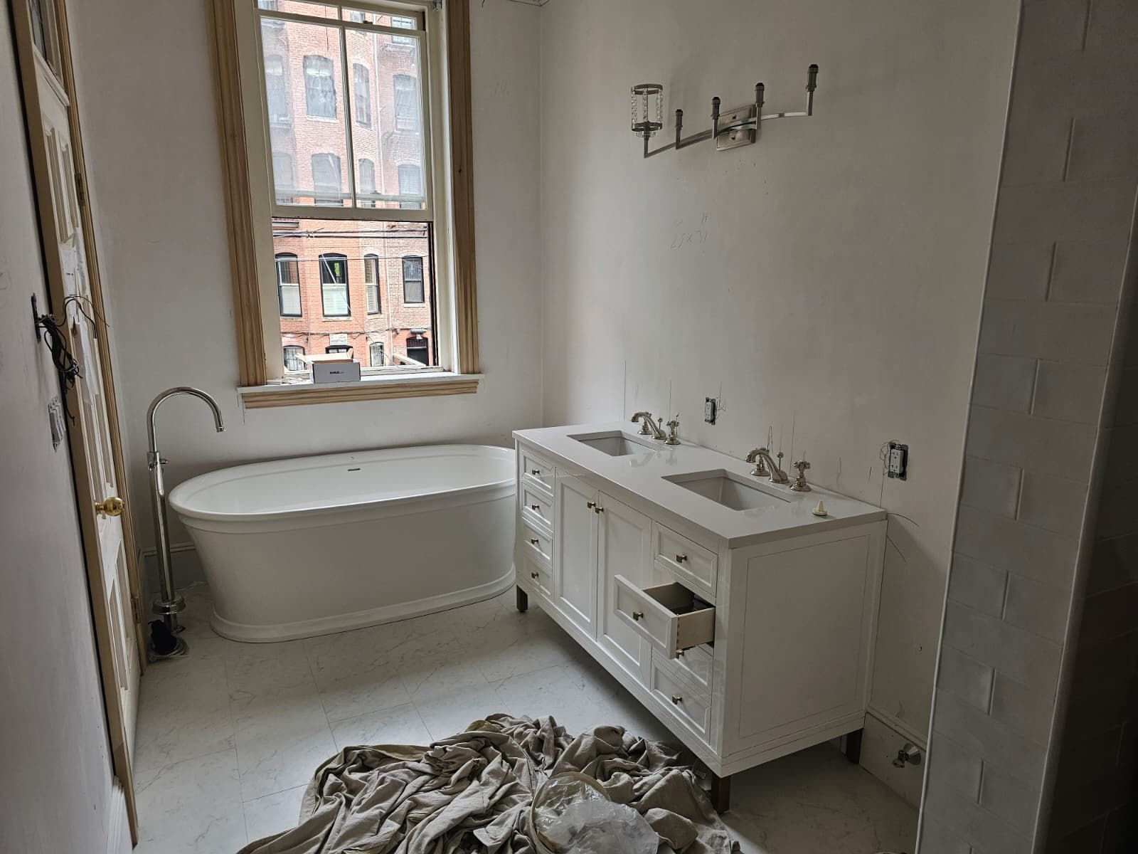 Bright bathroom with a freestanding tub, double vanity, and unfinished floor near a window.