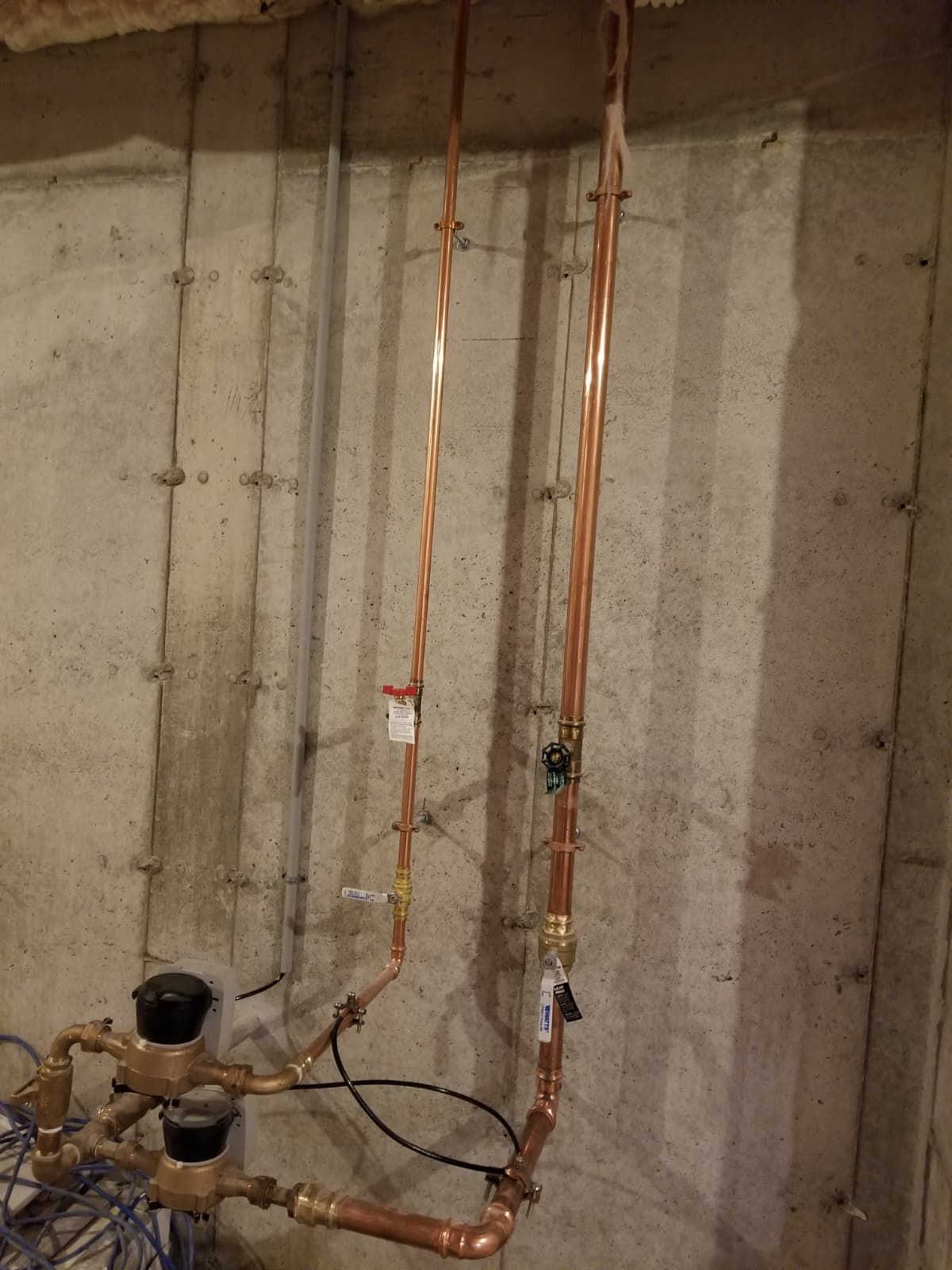 Copper plumbing pipes against a bare concrete basement wall with valves and fittings