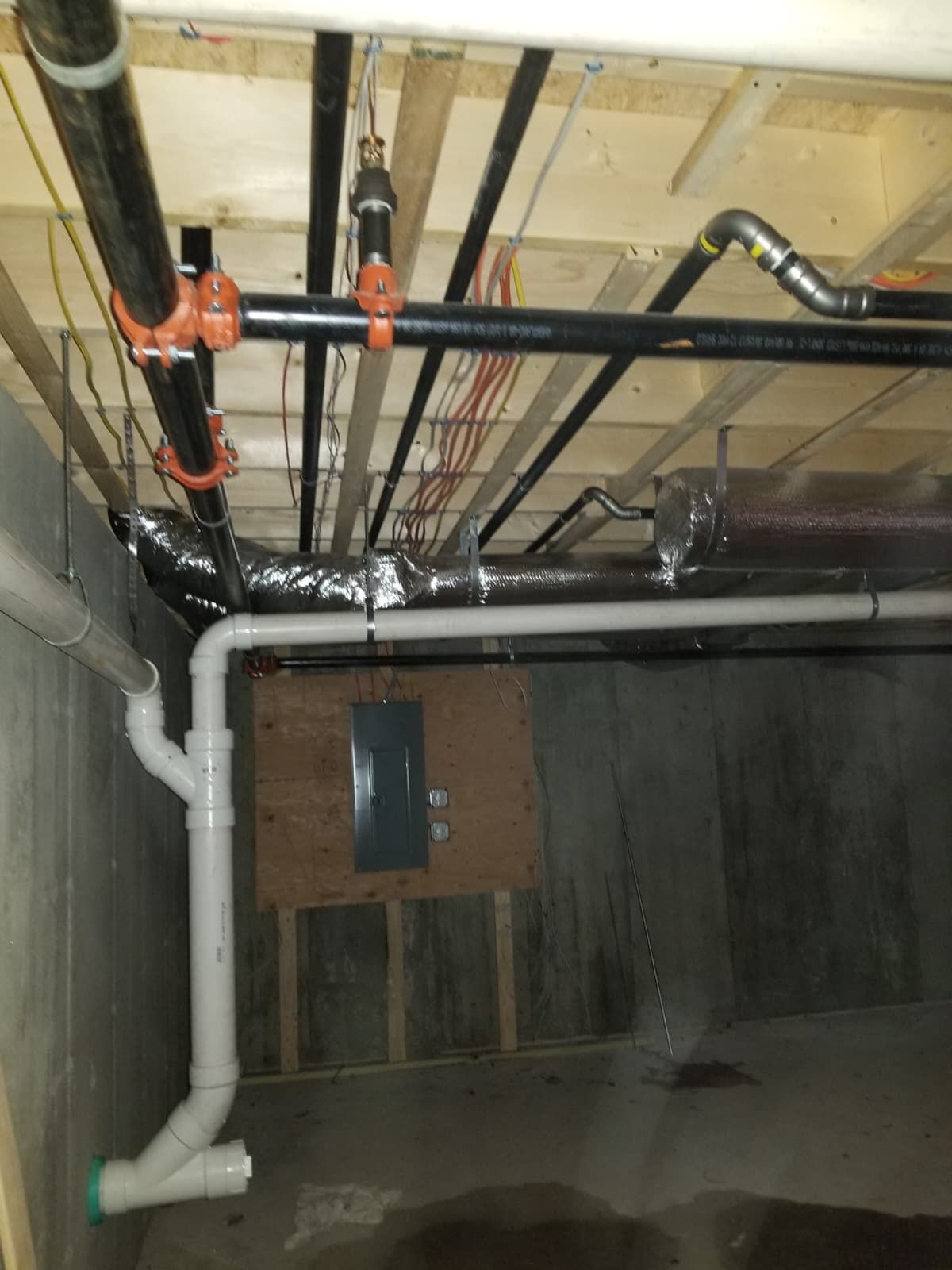 Basement ceiling with exposed pipes, orange valves, and ductwork above a concrete wall.