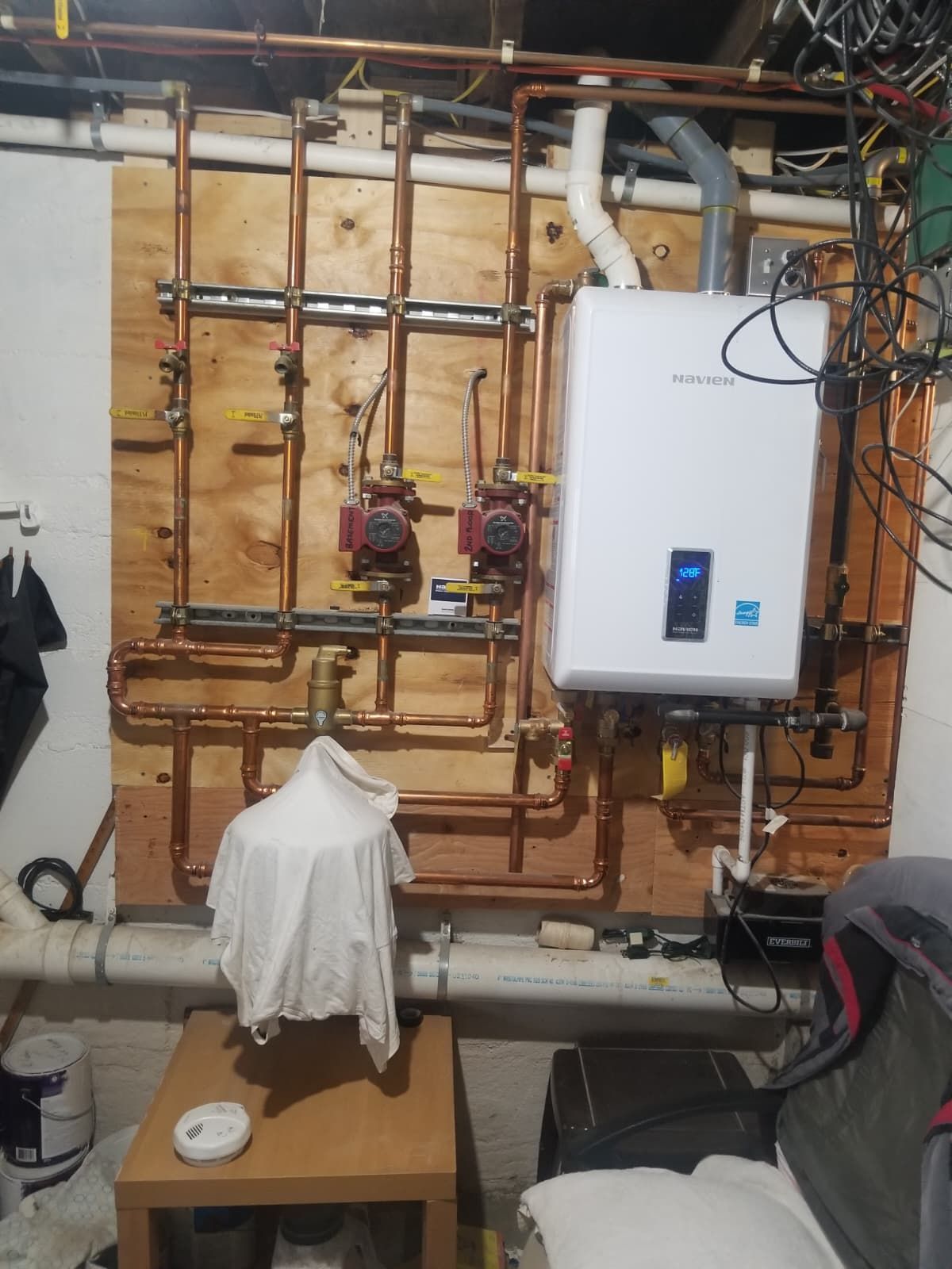 Basement utility wall with pipes, valves, and a white boiler unit mounted on wood framing.