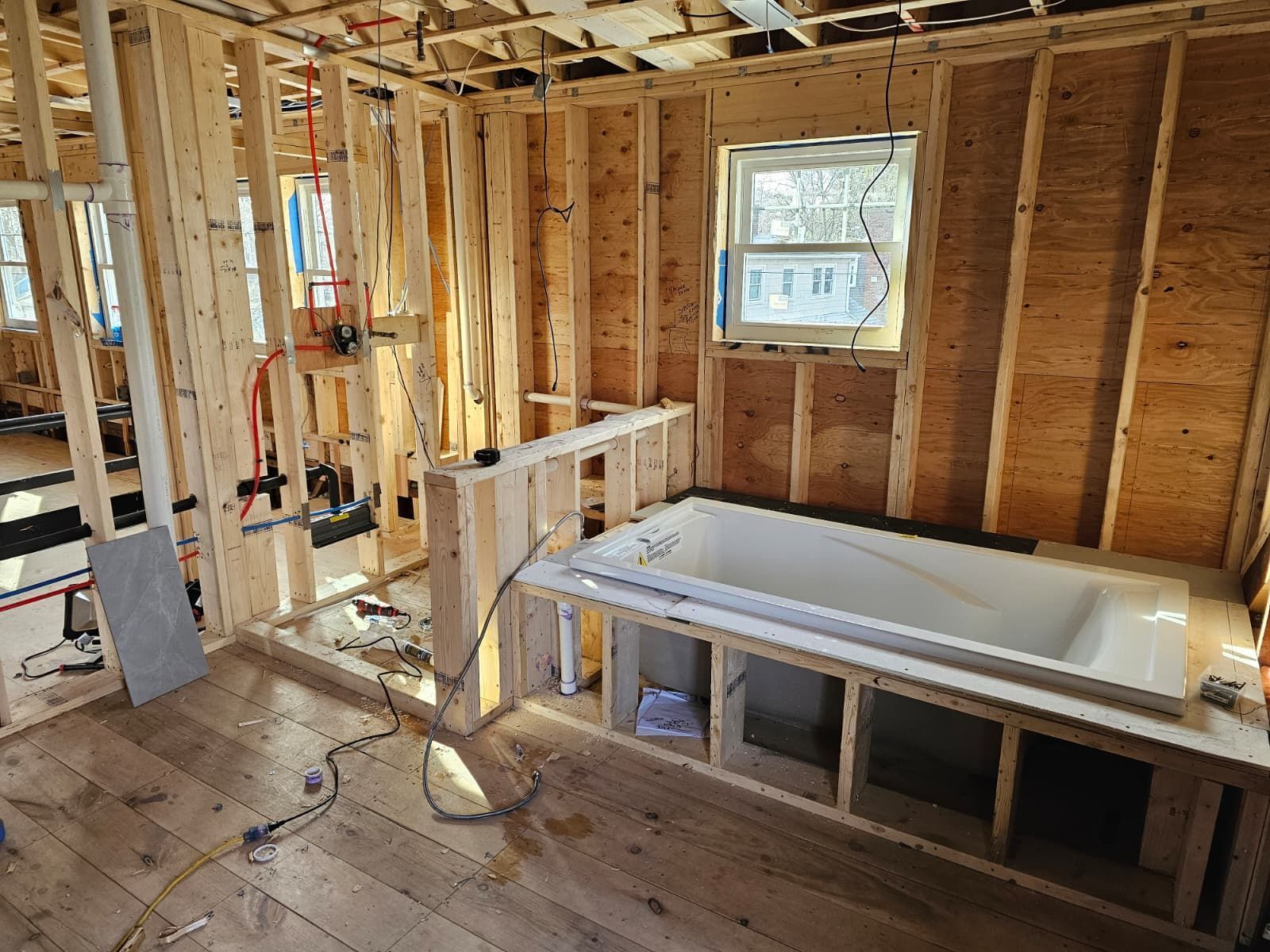 Interior under construction with exposed wooden framing, a window, and a built-in bench or tub platform.